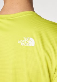 Lime zöld sportpóló, rácsos textúrával, hátul, a nyaknál fehér "The North Face" logóval.