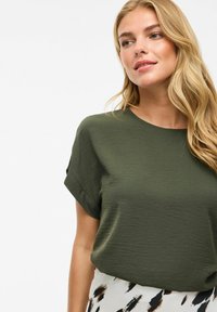 Haut vert olive à manches courtes avec un col rond et un tissu doux et texturé. Assorti à une jupe à motifs avec des accents noirs et beiges.