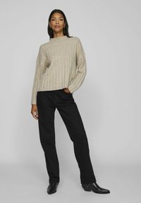 Beige geribd sweater met lange mouwen, opstaande kraag en een losse pasvorm, gecombineerd met zwarte rechte broek en puntige zwarte laarzen.