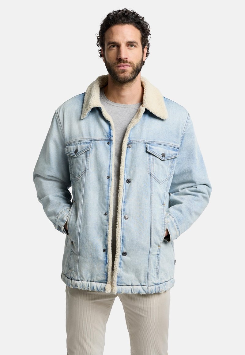 Ljusblå denimjacka med en krämfärgad fuskpälskrage, två bröstfickor och en dräkt nederkant. Avslappnad design med knappstängning.