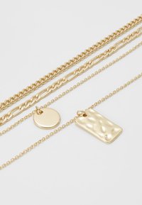 Collar de oro de múltiples capas que presenta diferentes estilos de cadena. Incluye un colgante circular liso y un colgante rectangular texturizado.