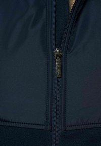 Donkerblauwe fleece hoodie met rits, voorzien van een gladde buitenkant en een gestructureerde voering, aangevuld met een metalen rits met merkdetails.