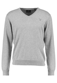 Šedý svetr s výstřihem do V a dlouhými rukávy, s žebrovanými manžetami a lemem. Na hrudi je malá nášivka. Vyrobeno z měkkého, lehkého materiálu.