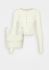 Ensemble en maille couleur crème comprenant un cardigan boutonné à manches longues et un crop top sans manches assorti avec un décolleté arrondi.