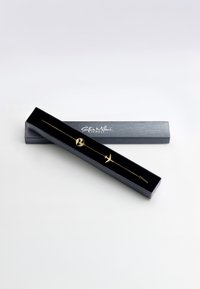 Guldbaserad armband med glob- och flygplansberlocker, visad i en svart låda med satininteriör. Enkel och elegant kedjedesign.