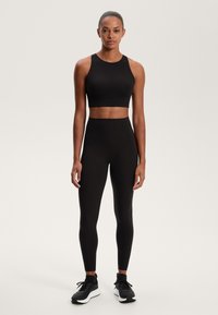 Črn atletski crop top v kombinaciji z visokimi črnimi leginami in črnimi športnimi copati. Gladek material z prilagojeno zasnovo in poenoteno silhueto.