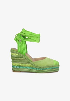 Espadrille vert avec une sangle tissée texturée et un capuchon en daim lisse. Présente des détails tissés en vert multi-ton sur la semelle compensée.