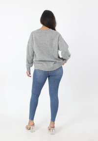 Lichtgrijze gebreide trui met een dropped shoulder, een gestructureerde stof en een ribgebreide zoom, gecombineerd met blauwe skinny jeans en sandalen met doorzichtige hakken.
