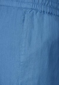 Lichtblauwe shorts gemaakt van zacht, gestructureerd materiaal met een elastische tailleband en zijzakjes. Stitching aan de randen is zichtbaar.