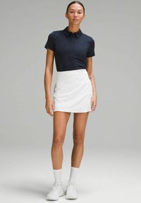 Mornarsko plava polo majica s ovratnikom i gumbima u kombinaciji s belim plisiranim suknjom. Model nosi bele tenisice i čarape.