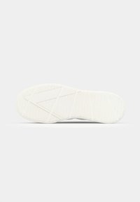 Semelle de chaussure en caoutchouc blanc avec motif de grip texturé et lignes diagonales géométriques, affichée à plat sur un fond gris clair.