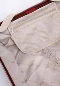 Intérieur ouvert d'une valise beige avec une doublure en tissu à logo, comprenant une poche en filet zippée et une sangle beige fixée à l'intérieur du couvercle.