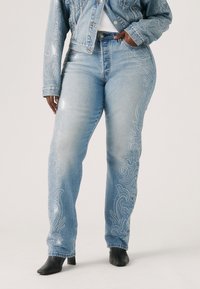 Jeans en denim bleu clair avec un motif orné de strass le long des coutures latérales, coupe droite et taille haute.