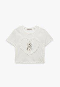 Hvid kortærmet crop t-shirt med et tekstureret blonde hjerte-design. Central illustration af en killing, detaljeret med en blå sløjfe. Blødt bomuldsstof.