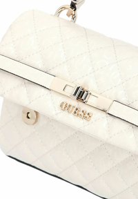 Sac Guess en cuir blanc matelassé avec logo métallisé, fermoir rectangulaire et attache de chaîne argentée.