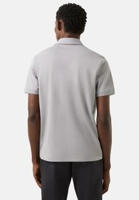 Gray polo shirt with short sleeves, soft texture, classic collar, and straight hem. Worn with dark trousers, minimal branding visible.