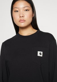 Schwarzes Langarm-T-Shirt aus Baumwolle mit einer Brusttasche und einem weißen Logolabel. Einfaches Design und reguläre Passform.