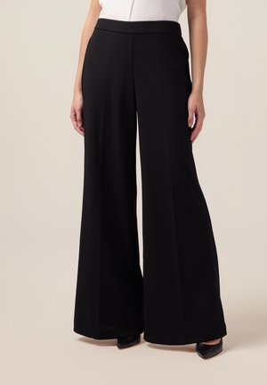 Pantaloni neri a gamba larga realizzati in tessuto morbido, con una vita alta e una vestibilità sartoriale che scende fino alle caviglie.