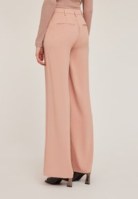 Pantalons larges en tissu rose doux, avec une texture lisse, des poches arrière et un design taille haute. Associés à des chaussures à talons.
