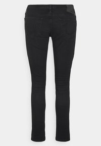 Jean skinny noirs en denim, dotés d'une texture lisse, de deux poches arrière et d'un discret patch logo à la taille.