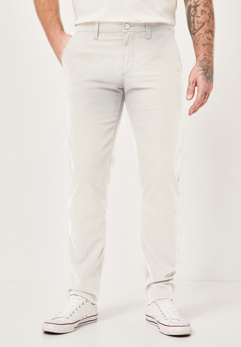 Hellegraue Baumwollchinos mit geradem Bein, ausgestattet mit Seitentaschen und einem geknöpften Bund. Kombiniert mit weißen Sneakern.