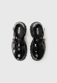 Sapatos de verniz pretos com um design Mary Jane, tira ajustável no tornozelo e sola de borracha chunky. Forro interior texturizado. Logótipo da marca visível.