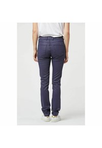 Donkerblauwe, strakke broek met een gladde textuur, voorzien van twee achterzakken en een middelhoge taille, in combinatie met witte sneakers.