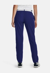 Mörkblå byxor med slät textur och avslappnad passform. Har bakfickor och resårmidja, i kombination med grå sportskor.