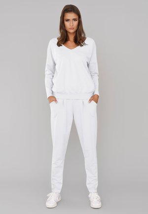 Biała bluza i pasujące dresy. W projekcie z dekoltem w serek, długie rękawy, elastyczne mankiety i kieszenie. Gładka tekstura, swobodny krój. Białe trampki.