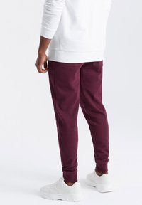 Burgunderfarbene Jogger aus weichem Stoff, mit schmaler Passform und seitlichen Taschen, kombiniert mit weißen Sportschuhen.