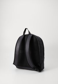 Zaino nero con spallacci imbottiti, tessuto testurizzato e design trapuntato su un lato. Nessuna ferramenta visibile o tasche esterne.