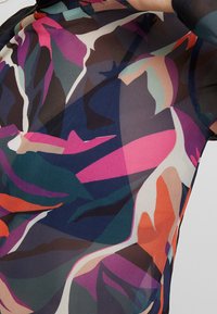 Flerfärgad mesh-top med djärva, abstrakta blommönster i nyanser av rosa, grön, marinblå och orange med en semi-transparent textur.