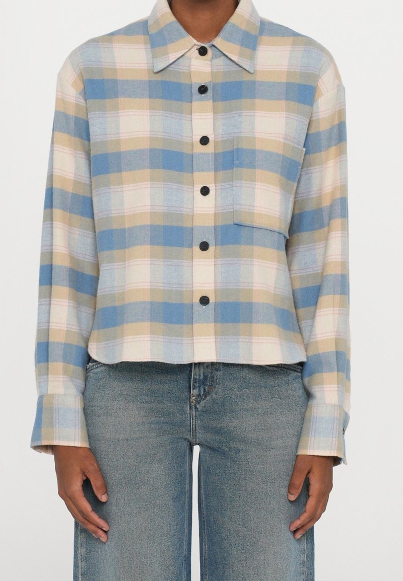 Chemise en flanelle légère à carreaux dans des tons de bleu, beige et rose. Comprend une fermeture à boutons sur le devant, un col, des manches longues et une poche poitrine.