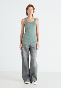 Grønn tanktop med blondekant, kombinert med grå utsvingte jeans og hvite sneakers, med en avslappet passform og myk tekstur.