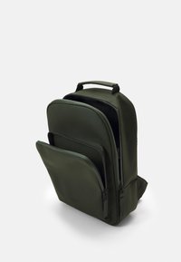 Grön nylonryggsäck med rundad form, dubbla dragkedjefack och en framficka. Har ett handtag upptill för enkel bärning.