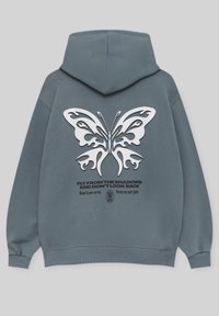 Sweat à capuche bleu-gris avec un grand motif papillon blanc et le texte « Envole-toi des ombres et ne regarde pas en arrière » au dos.