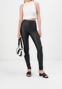 Černé skinny kalhoty s vysokým pasem vyrobené z elastického materiálu, doplněné bílým crop topem. Dopňky zahrnují malou černobílou kabelku.