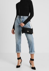 Top nero a coste a maniche lunghe, jeans blu chiaro con risvolto, borsa a tracolla nera con texture e décolleté neri con cinturini alla caviglia.