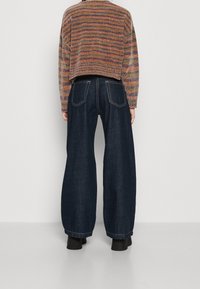 Geknipte, multicolored trui met horizontale strepen, gecombineerd met luchtige, donkerblauwe denim broeken met achterzakken en zichtbare stiksels.