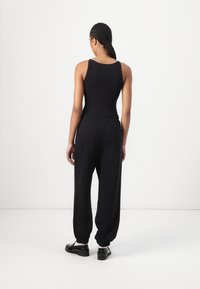 Black ribbed tank top paired with loose-fitting black sweatpants, featuring elastic cuffs and a back pocket detail. Smooth fabric texture.