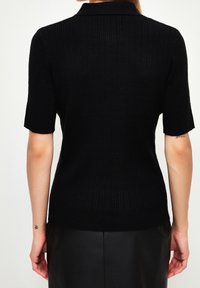 Haut noir côtelé à manches courtes avec col, présentant une coupe ajustée et une texture lisse, vu de dos.