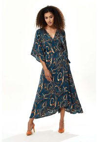 Maxi dress in teal fabric features an abstract swirl pattern in orange and cream, with a V-neck, wide sleeves, and a tied waist.