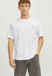 Hvid bomulds t-shirt med en afslappet pasform, der har et lille sort skalle-design på brystet. Korte ærmer og rund halsudskæring.