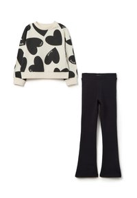 Sweat-shirt avec imprimé cœur noir sur fond crème, avec des poignets côtelés, associé à des leggings évasés noirs unis, le tout en tissu doux.