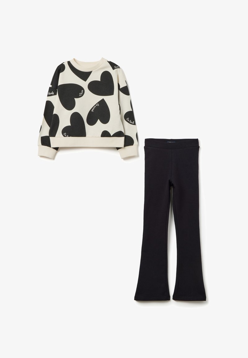 Sweat-shirt avec imprimé cœur noir sur fond crème, avec des poignets côtelés, associé à des leggings évasés noirs unis, le tout en tissu doux.