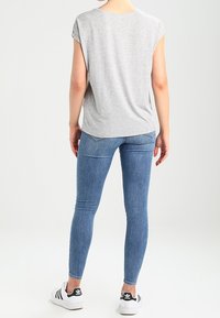Gray short-sleeve t-shirt with rolled cuffs, paired with blue skinny jeans and black sneakers featuring white accents. Back view.