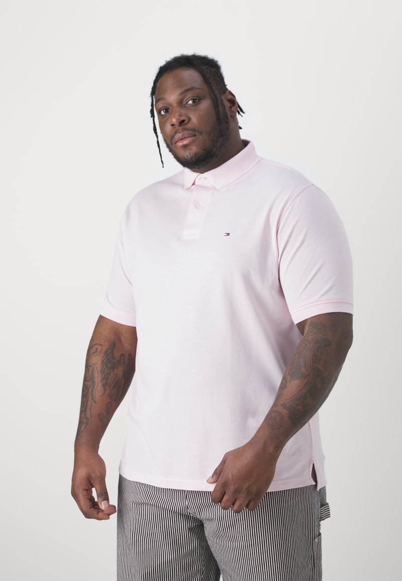 Polo shirt rosa chiaro con colletto, maniche corte e un piccolo logo sul petto. Tessuto liscio, vestibilità classica e spacchetti laterali all'orlo.