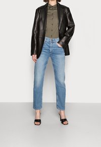 Blazer de cuero negro, camisa de botón verde oliva, jeans rectos de mezclilla azul claros y zapatos de tacón abiertos negros. Un look simple y estructurado.