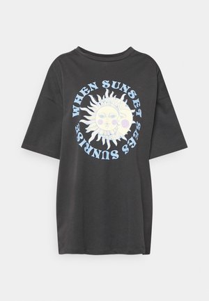 Sort oversized T-shirt med en sol og måne grafik og teksten "WHEN SUNSET SEES SUNRISE" i lyseblåt omkring den.