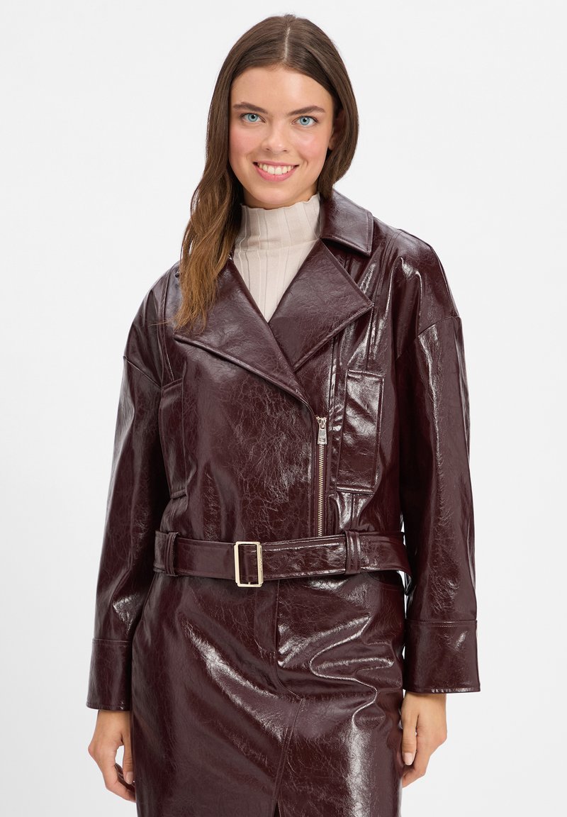 Giacca in finta pelle burgundy con ampi risvolti, chiusura frontale con zip e vita cintata. Presenta una finitura lucida e una vestibilità rilassata.